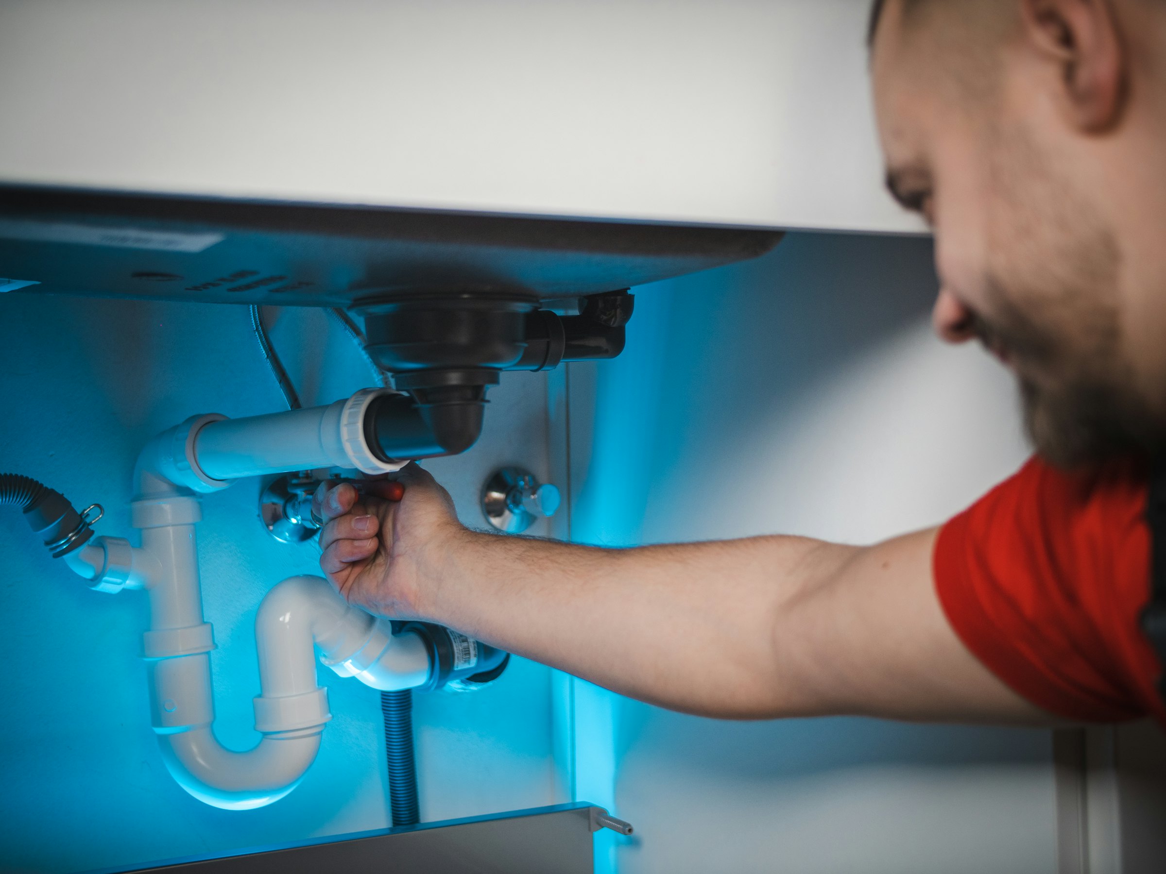 Sanitärinstallateur schliesst den Siphon unter einem Lavabo an